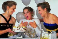 photo of a North American birthday party--two women are giving their girlfriend a cake with candles and wrapped presents