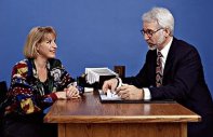 photo of a gray-haired man in a business suit sitting at a desk interviewing a younger woman
